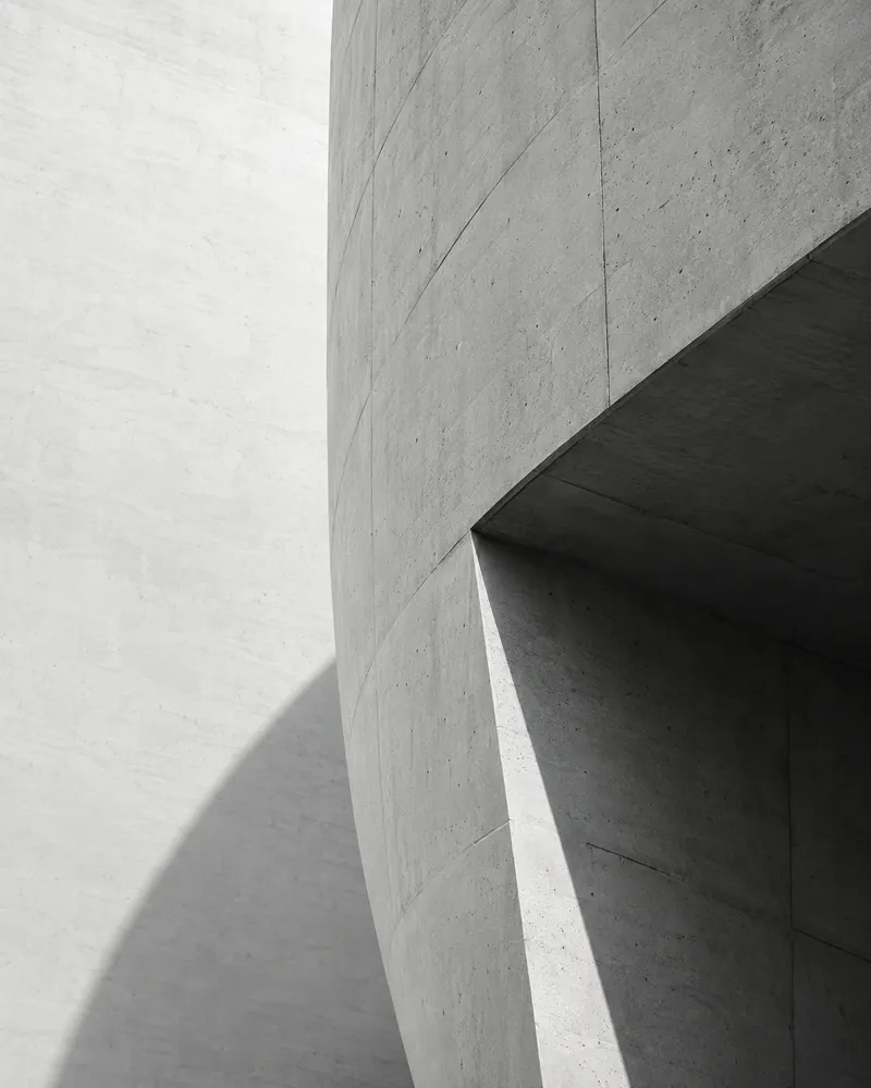 Curved concrete surfaces meeting a sharply angled opening in natural light.